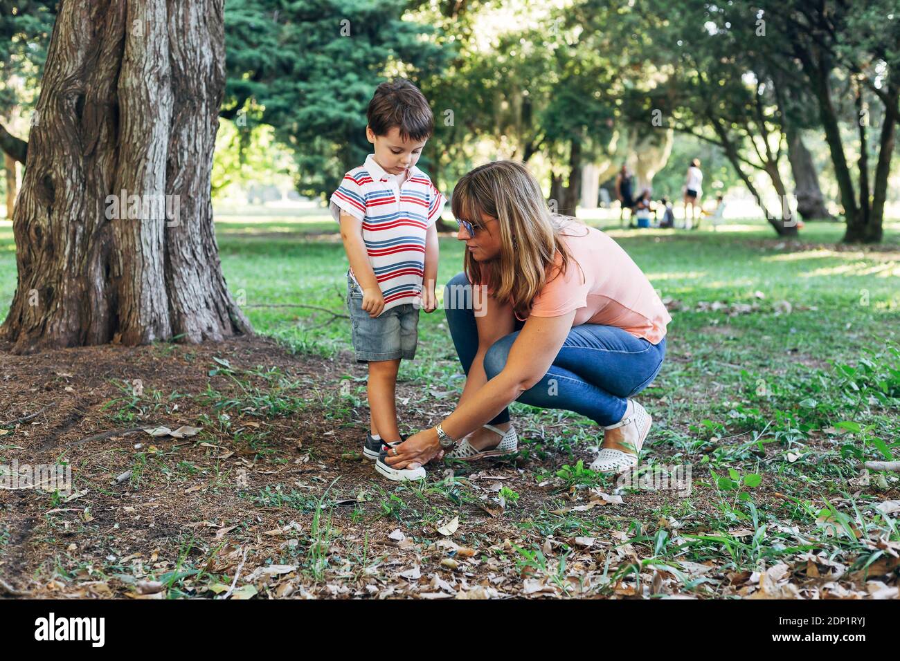 Mamma che lega le sneakers al suo figlio piccolo. Madre con il bambino nel mezzo del parco forestale. Foto Stock