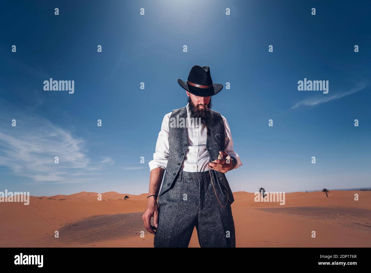 Uomo con la barba e hat nelle dune del deserto del Marocco controllando il tempo Foto Stock