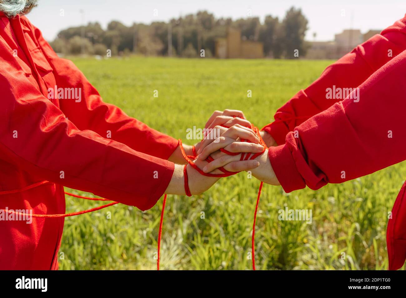 Vista di ritaglio di giovane coppia vestita di rosso che si esibisce sopra un campo con una stringa rossa Foto Stock