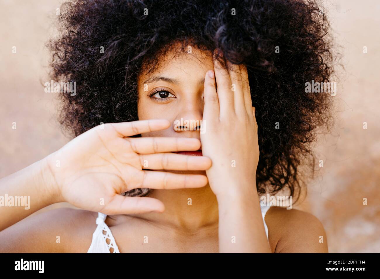 Ritratto di donna afroamericana con i capelli afro con le mani sul viso di fronte al vecchio muro urbano di Granada, Spagna Foto Stock