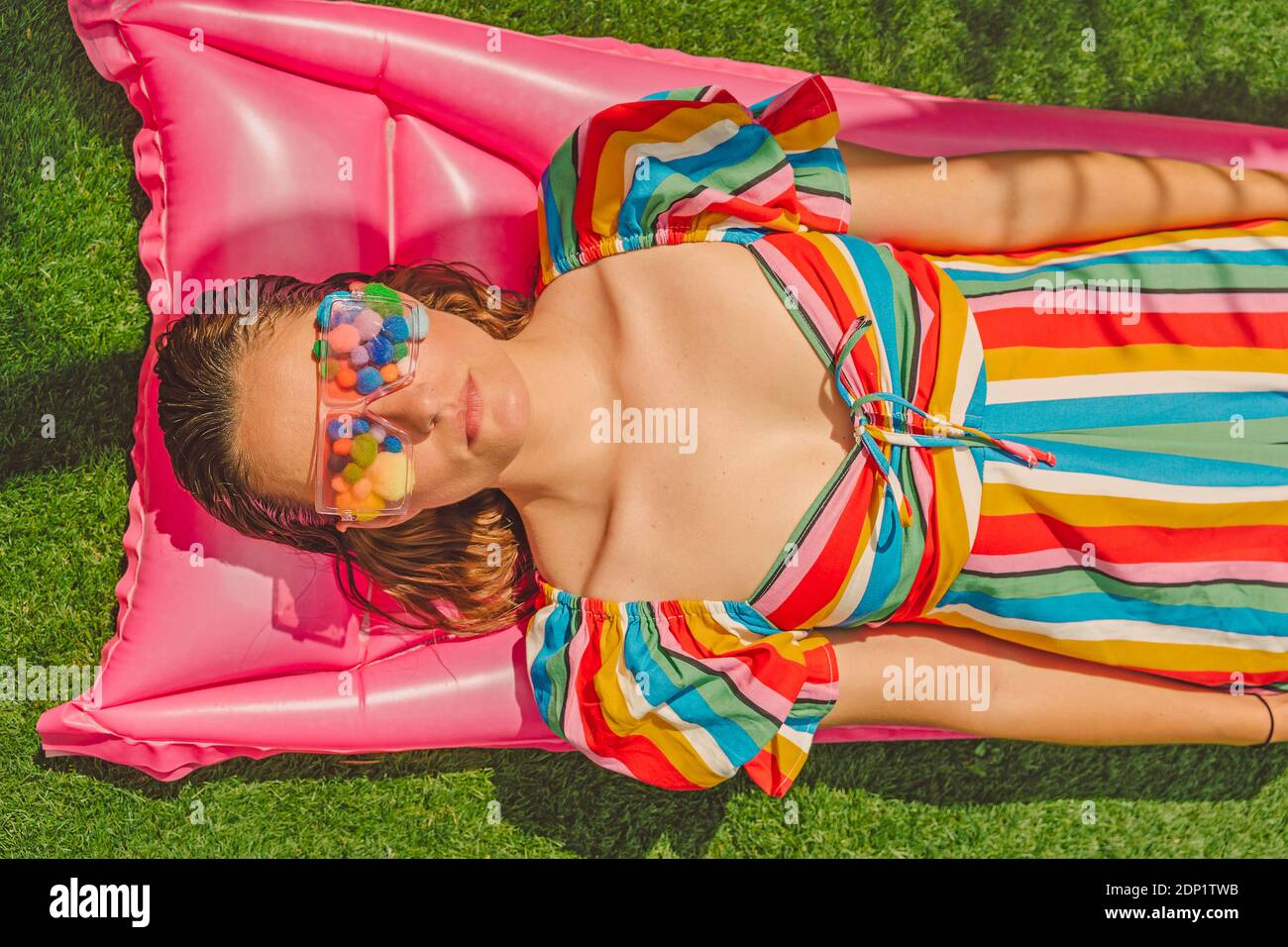 Ritratto di donna che indossa occhiali con pom pom colorati copertura i suoi occhi rilassandosi sul letto d'aria rosa Foto Stock