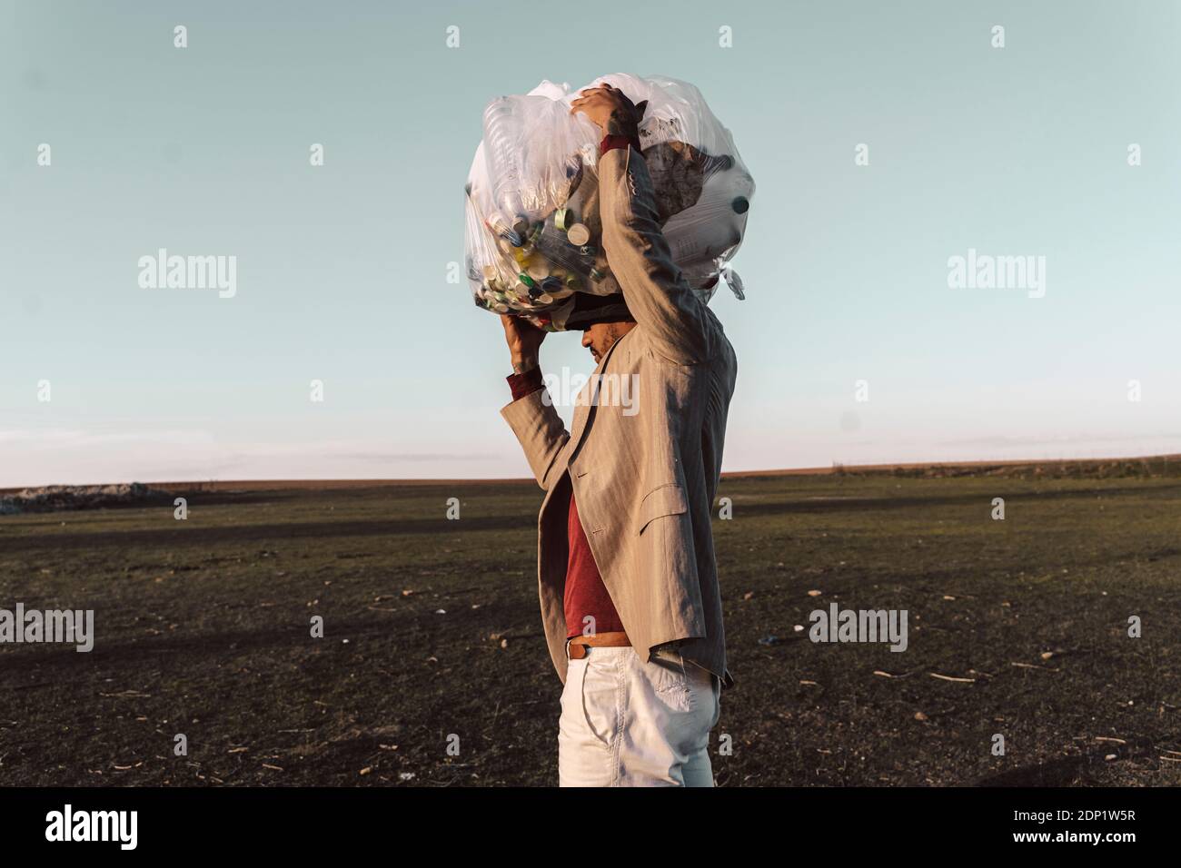 Giovane uomo che porta borsa con bottiglie di plastica sulla sua testa in terra sterile Foto Stock
