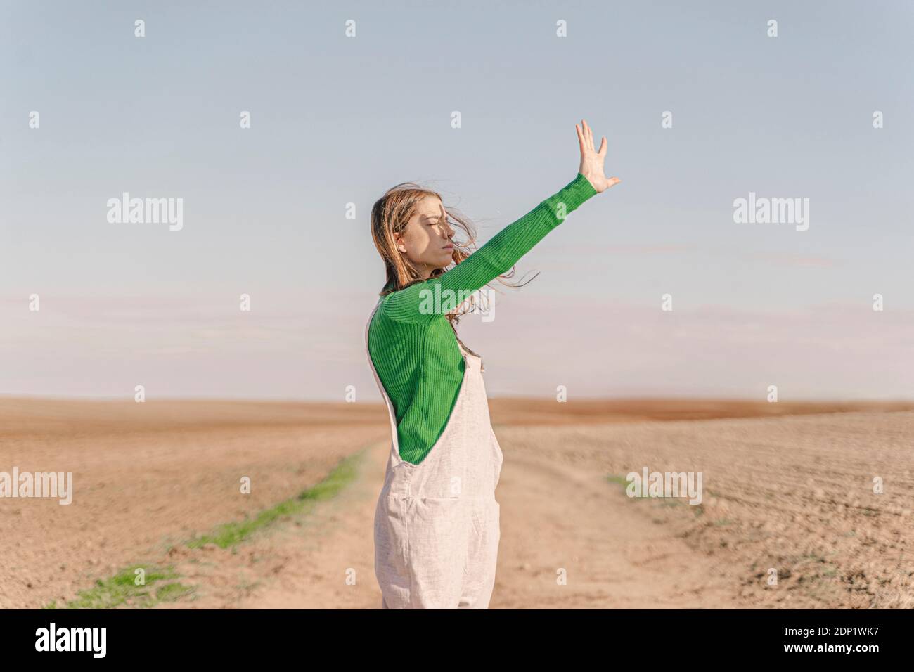 Giovane donna in piedi su campo asciutto, schermando gli occhi Foto Stock