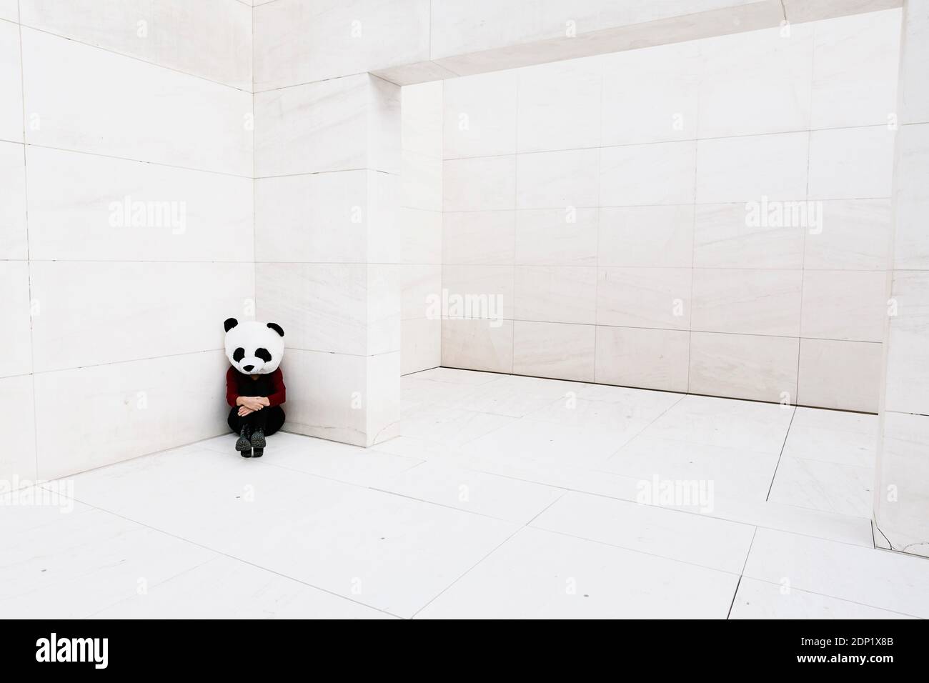 Donna triste che indossa una maschera da panda seduta ad angolo contro il muro Foto Stock