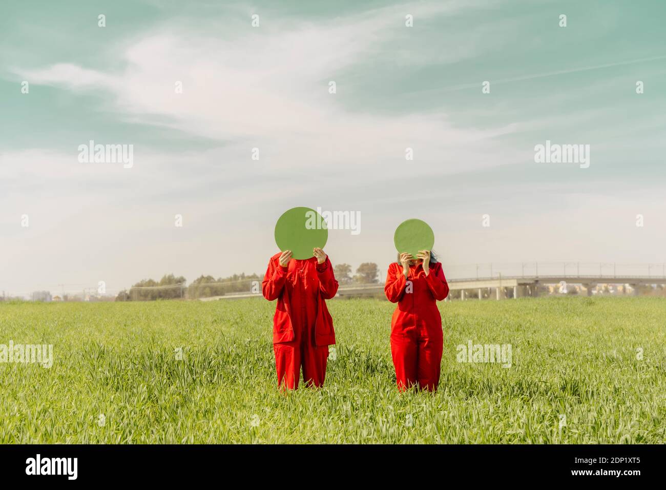 Giovane coppia che indossa tute rosse in piedi su un campo nascosto facce dietro il cerchio verde Foto Stock