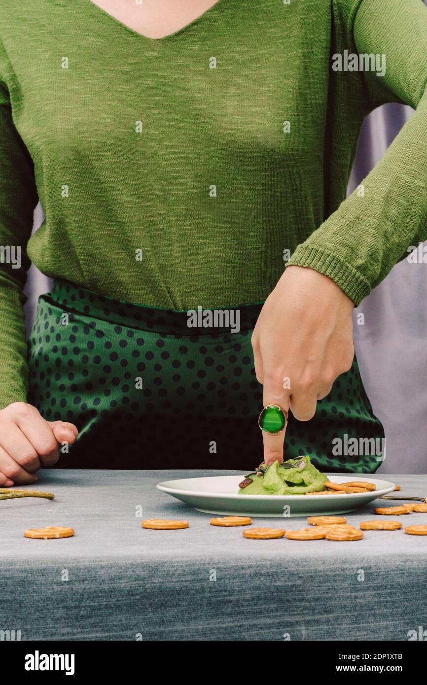 Primo piano di donna con dito in guacamole sul tavolo a. casa Foto Stock
