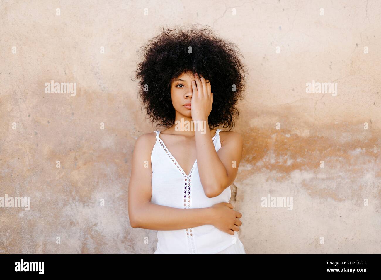 Ritratto di donna afroamericana con i capelli afro con le mani sul viso di fronte al vecchio muro urbano di Granada, Spagna Foto Stock