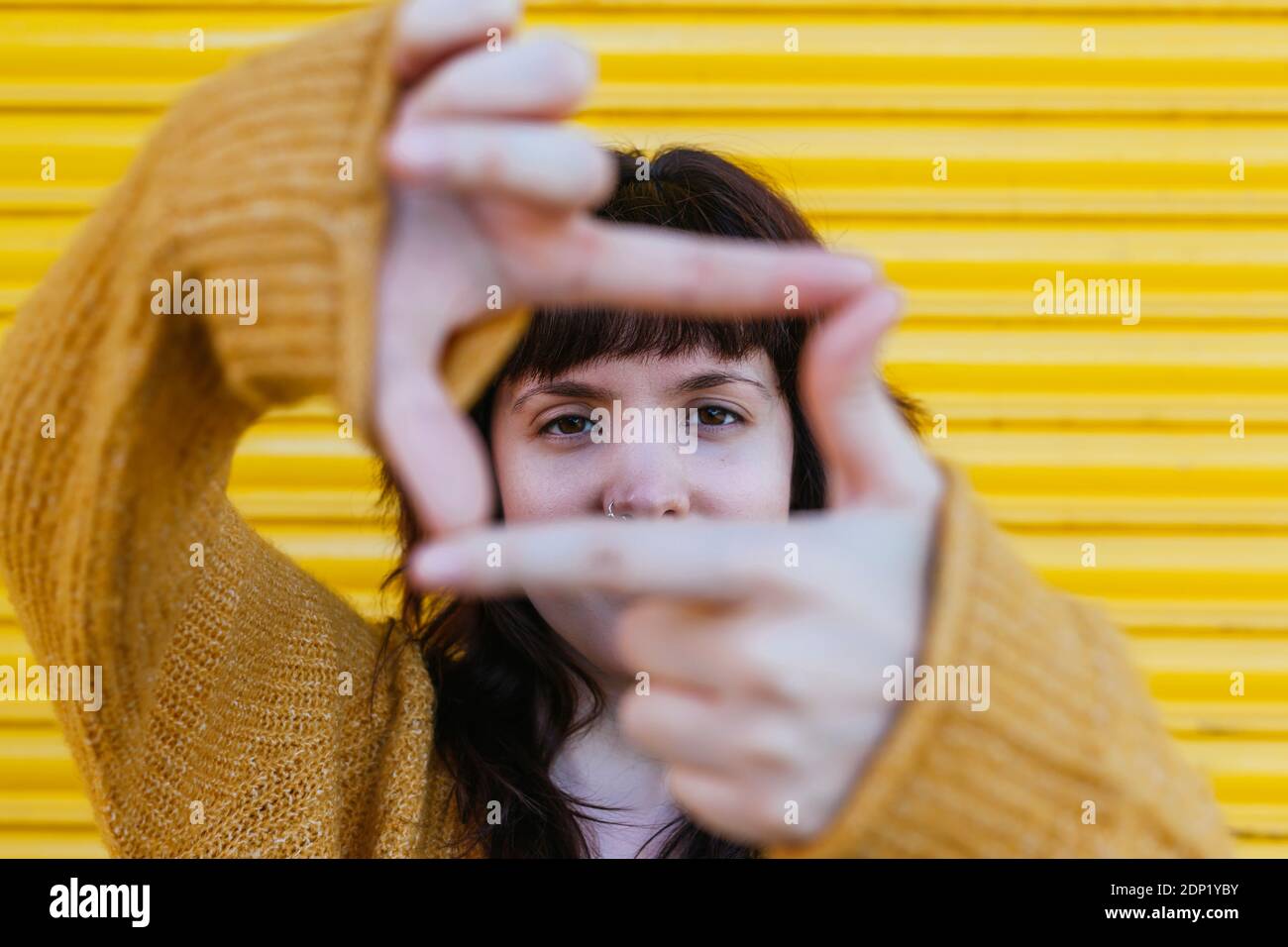 Donna bruna che fa il movimento della cornice del dito contro l'otturatore Foto Stock