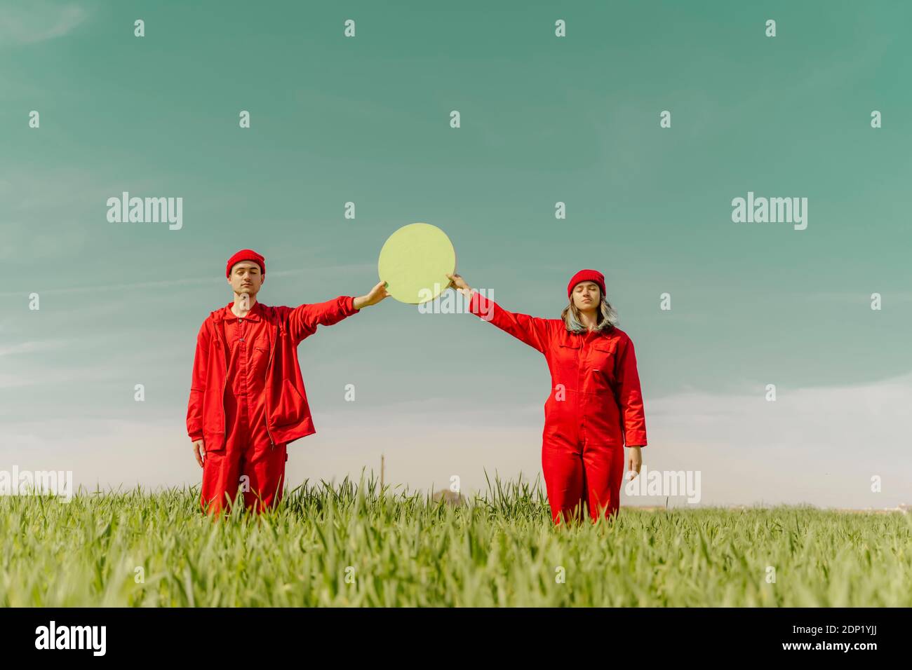 Giovane coppia che indossa tute rosse in piedi su una tenuta di campo cerchio verde Foto Stock