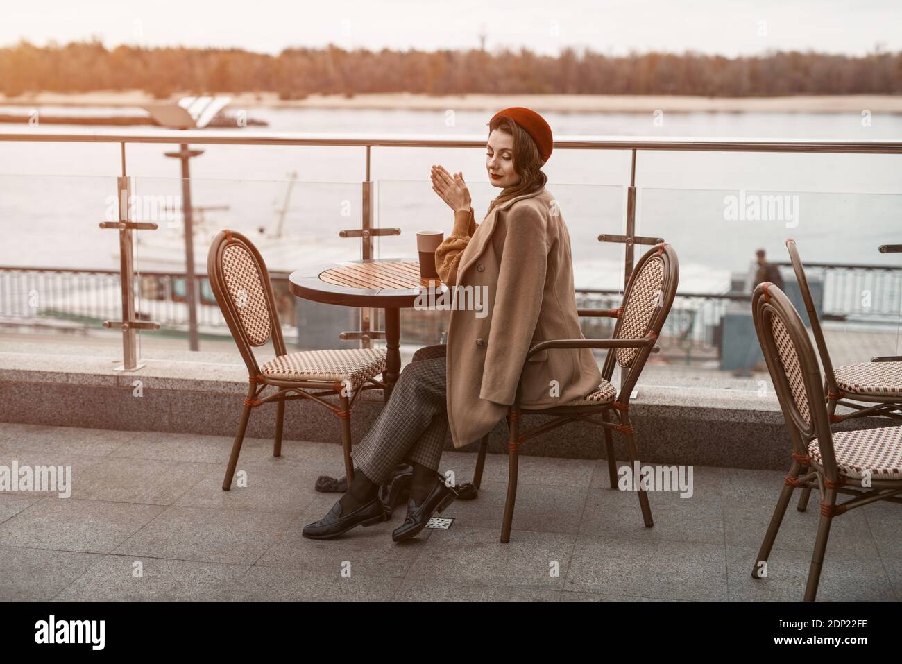 Piano generale di una giovane donna parigina premurosa con una tazza di caffè sul tavolo che indossa berretti rossi seduti sulla terrazza del ristorante o della caffetteria. Autunno Foto Stock