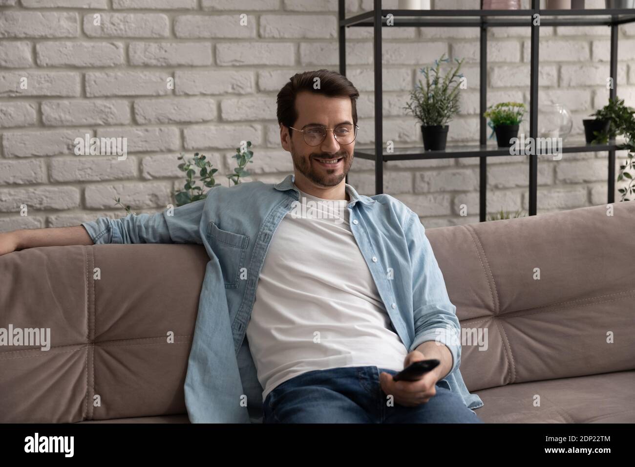Ragazzo sorridente che si riposa prima che lo schermo della tv tenga il telecomando Foto Stock
