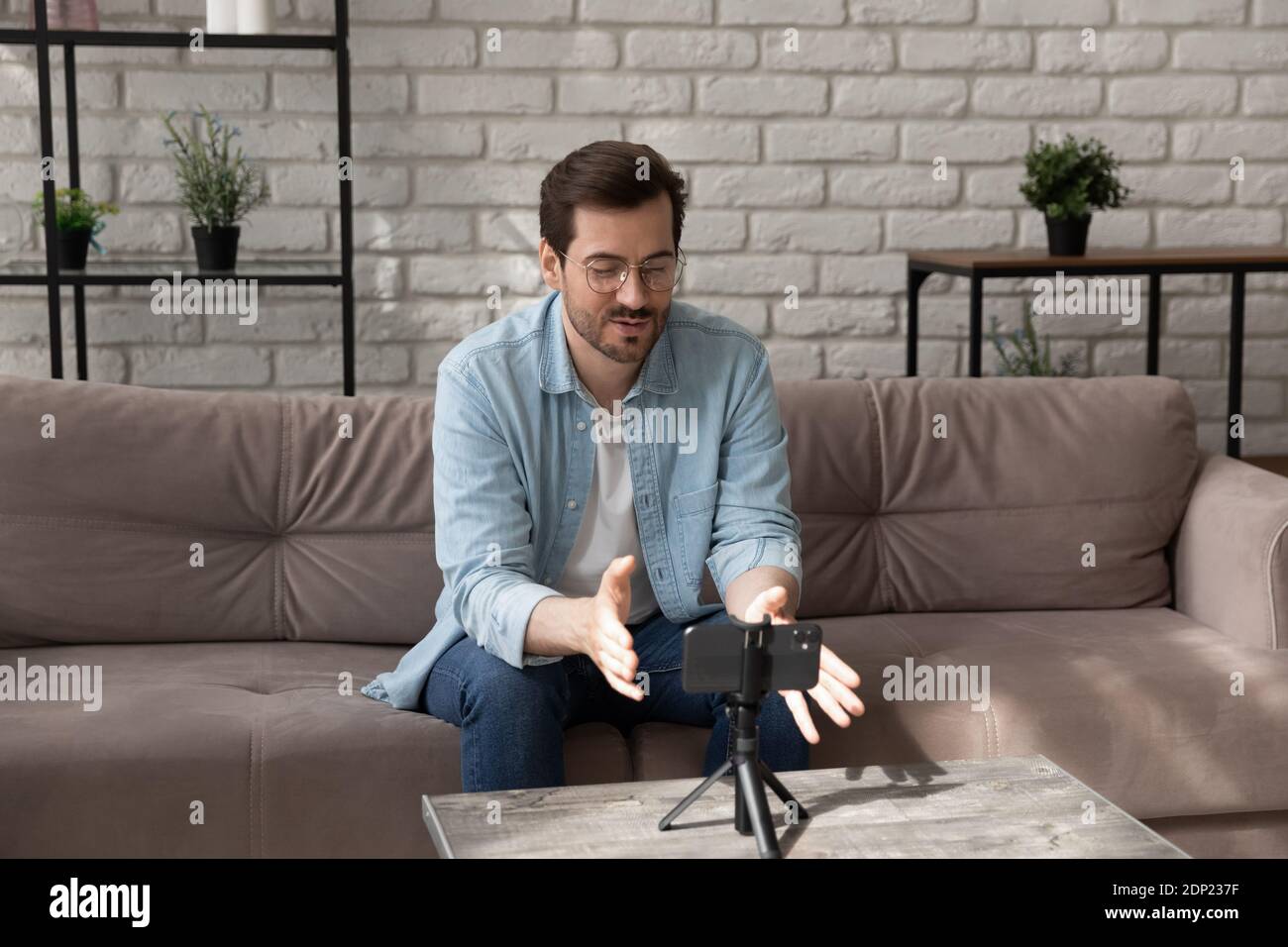 Giovane uomo sicuro che comunica con i colleghi utilizzando il cellulare sul treppiede Foto Stock