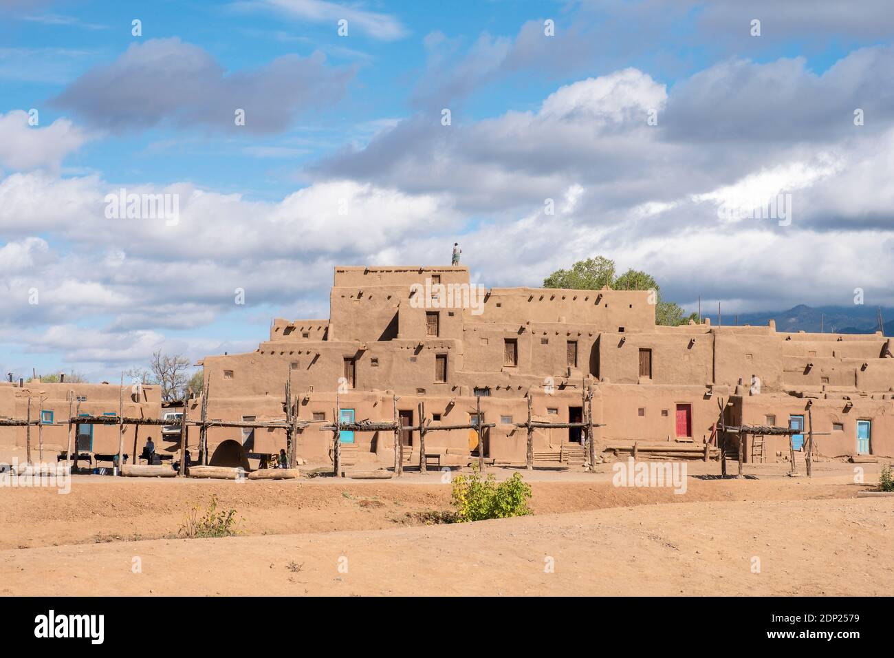 Uomo che pulisce il tetto di case in mattoni di fango di adobe nello storico villaggio dei nativi americani di Taos Pueblo, New Mexico, USA. Un sito patrimonio dell'umanità dell'UNESCO. Foto Stock