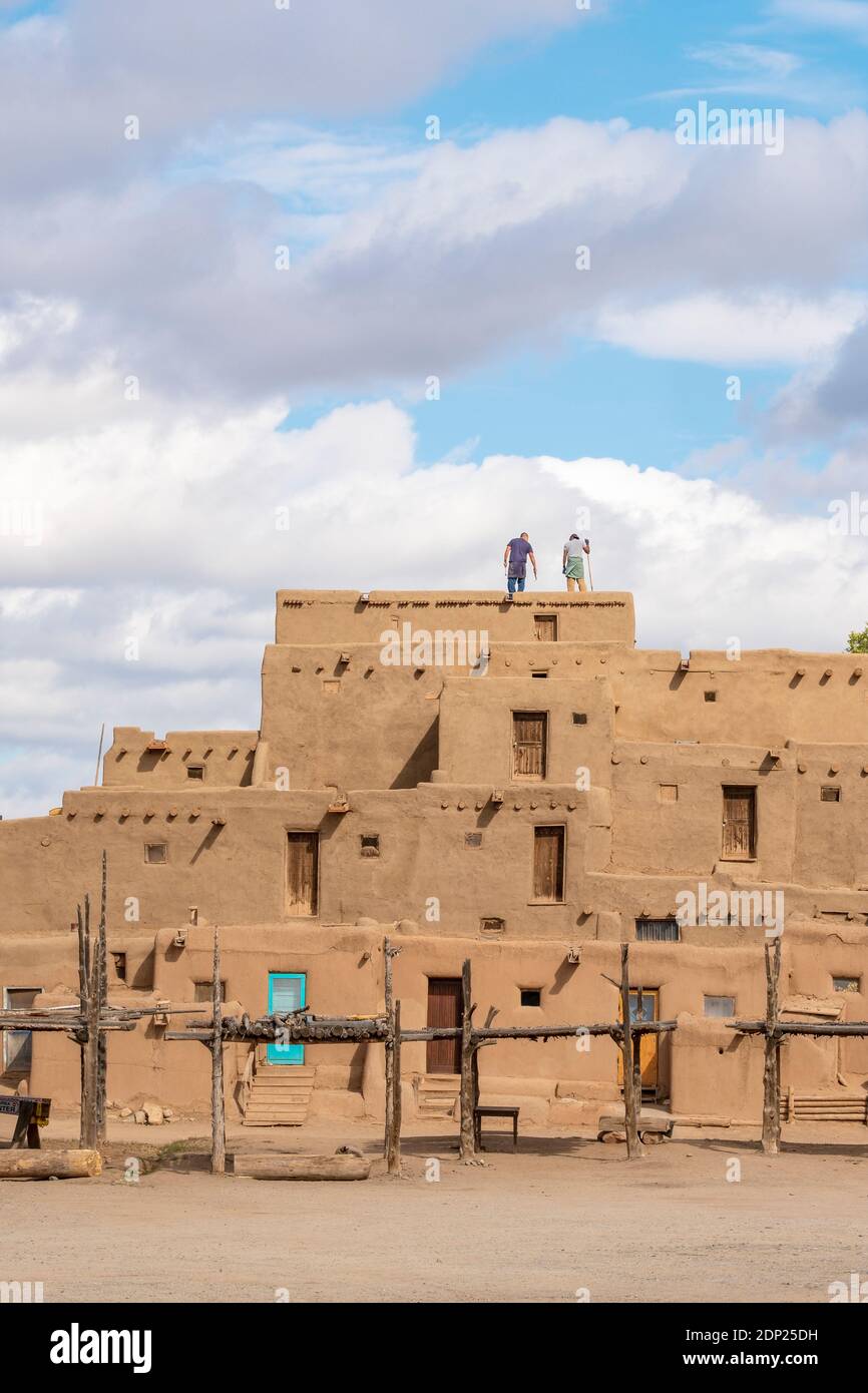 Uomini che puliscono il tetto di case in mattoni di fango di adobe nello storico villaggio dei nativi americani di Taos Pueblo, New Mexico, USA. Un sito patrimonio dell'umanità dell'UNESCO. Foto Stock