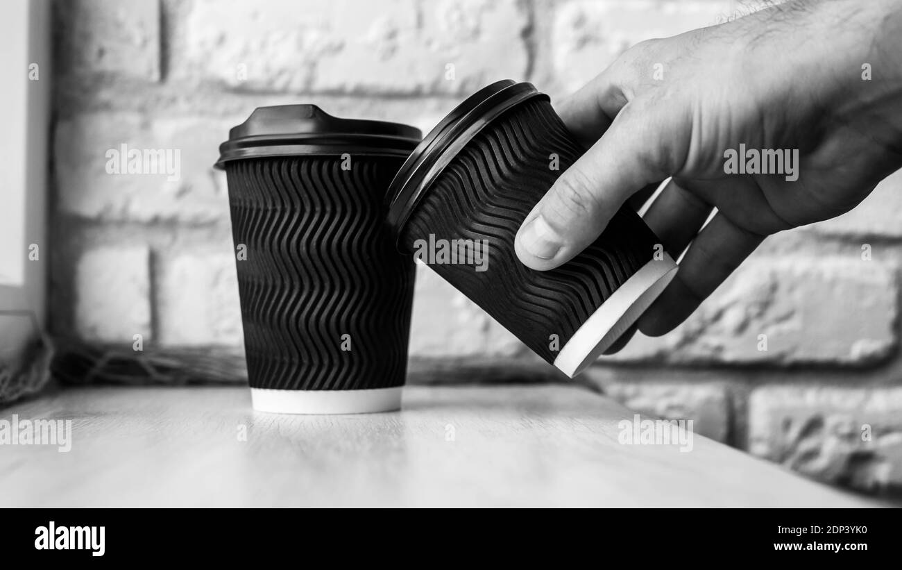 Un uomo fa un toast caffè, un bicchiere di caffè, cappuccino in mano, caffè nero in un bicchiere di plastica, primo piano, foto in bianco e nero. Contro il backgr Foto Stock