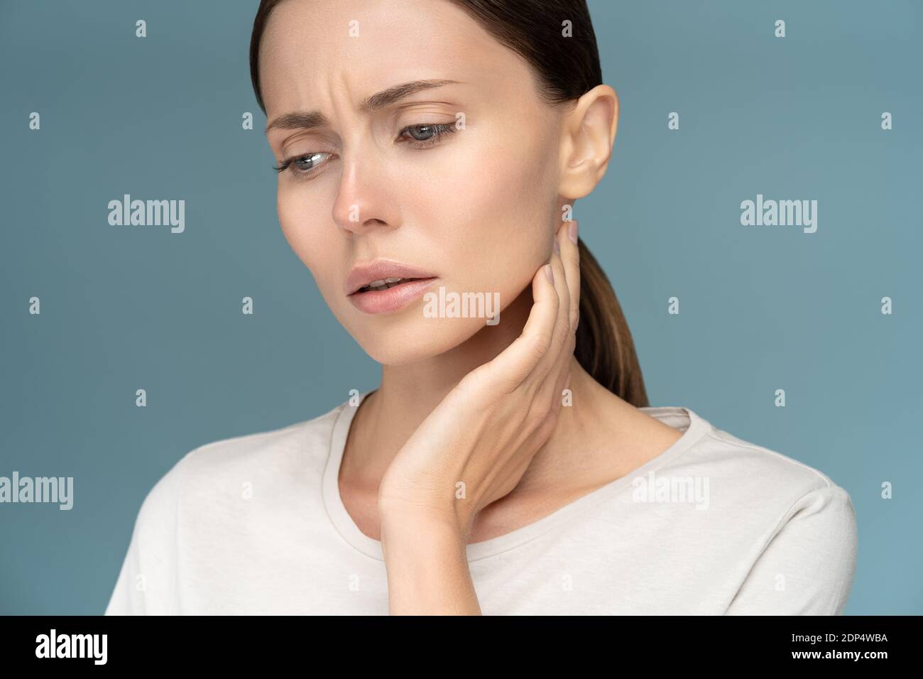 Closeup di malata donna triste controllo linfonodi, colto, sofferente di problemi alla gola, isolato su sfondo blu studio Foto Stock