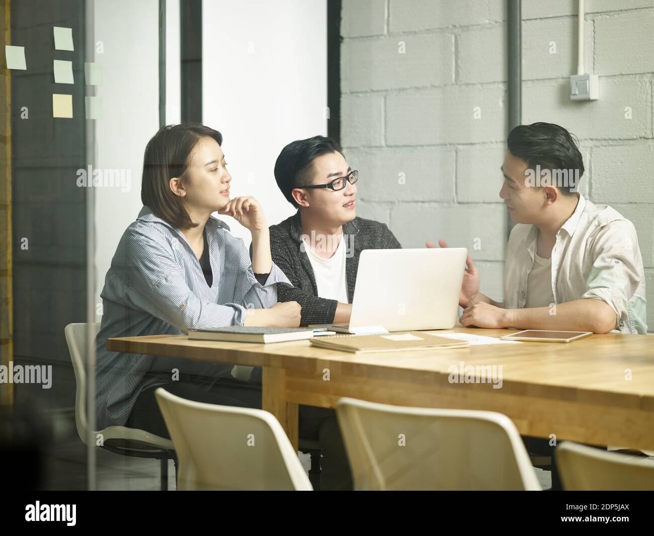 tre giovani imprenditori asiatici si riunono in ufficio discutendo di business utilizzando computer portatile Foto Stock