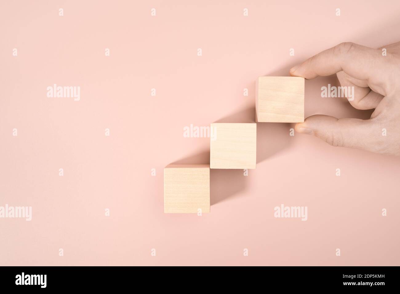 Business concept processo di successo di crescita, chiudere uomo mano che dispone legno blocco impilando come scala passo su sfondo rosa, copia spazio. Foto Stock