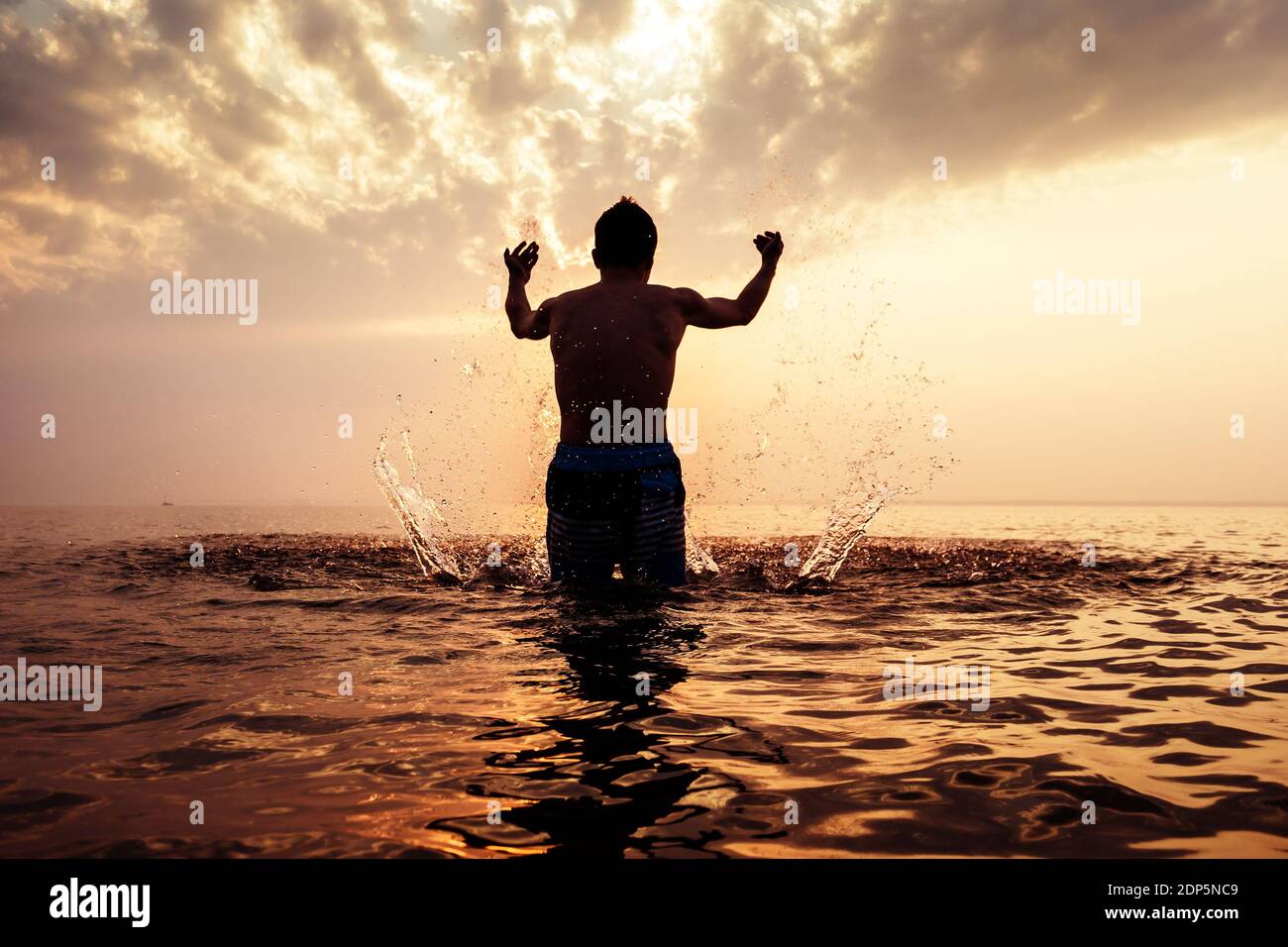 Tone Photo of Happy Man Silhouette con schizzi nel Acqua sullo sfondo del tramonto Foto Stock