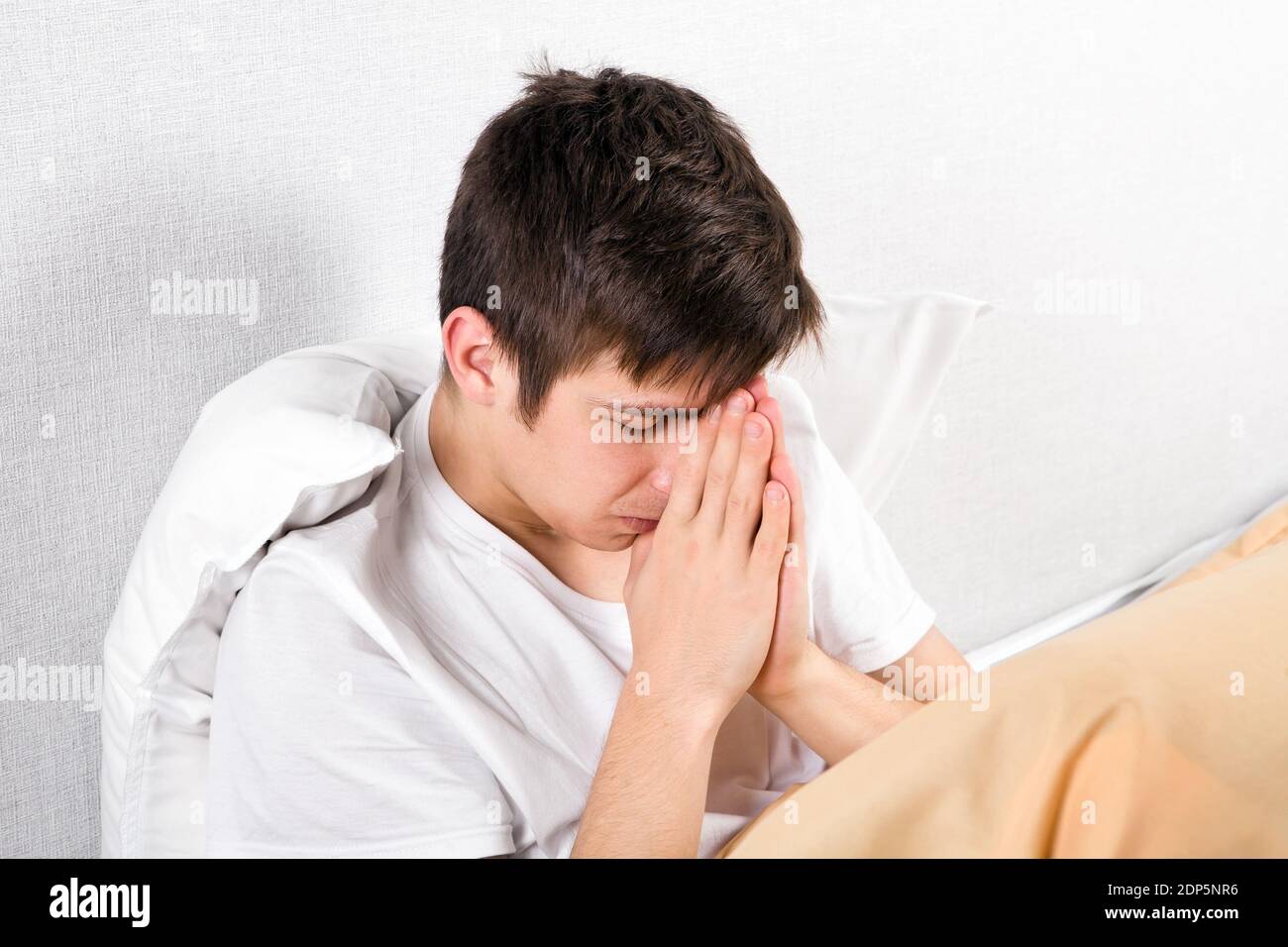 Giovane uomo che prega sul letto a casa Foto Stock