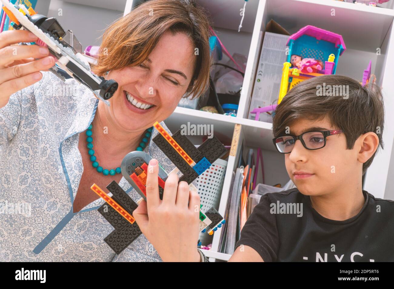 Elegante, madre caucasica ama giocare con suo figlio. Volano piccoli aerei fatti di mattoni di plastica. Donna ride. Attività moderna per famiglie con bambini. Foto Stock