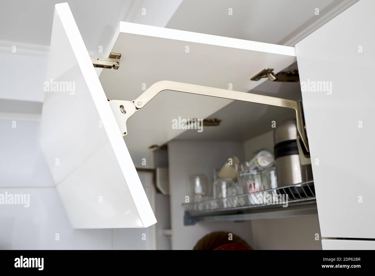 Parte degli interni della cucina contemporanea. Aperto armadio da cucina orizzontale bianco con piatti e bicchieri su ripiano. Sollevamento porta armadio cucina Foto Stock