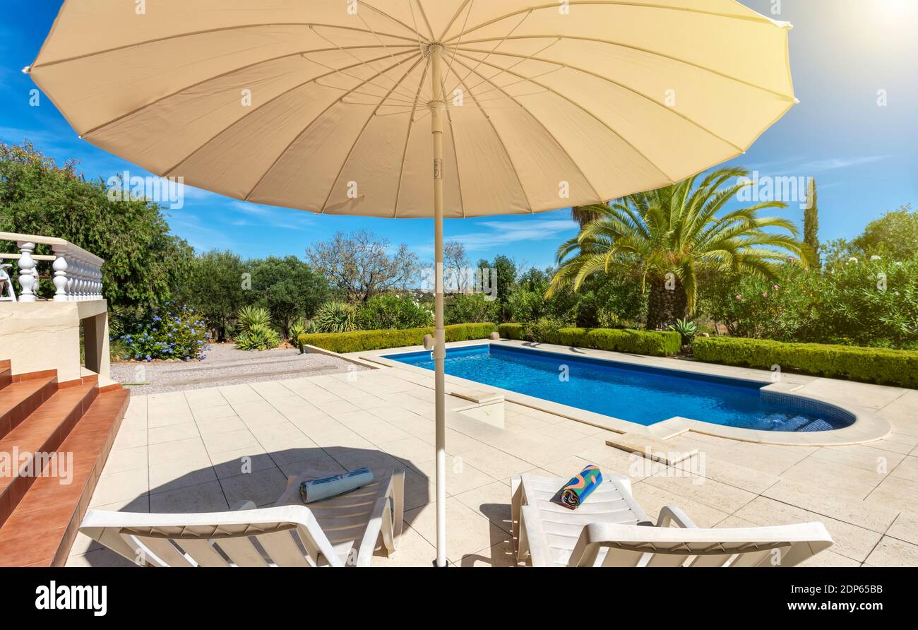 Piscina di lusso nel giardino di una villa privata, sedia pensile con cuscini per turisti, in estate. Portogallo, Algarve. Foto Stock