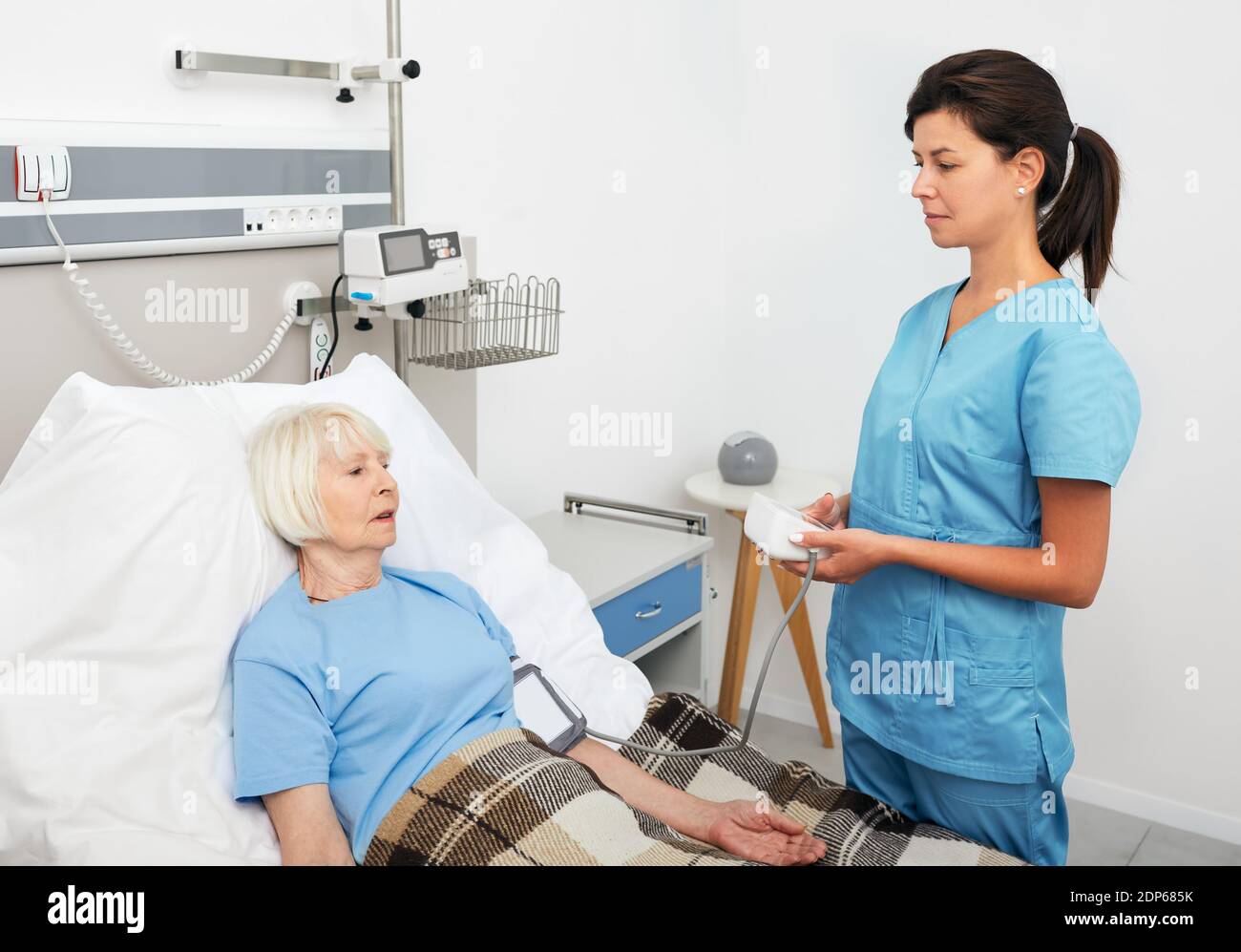 L'infermiere geriatrico misura la pressione di una paziente anziana che si trova su un letto ospedaliero. Prevenzione e trattamento dell'ipertensione Foto Stock