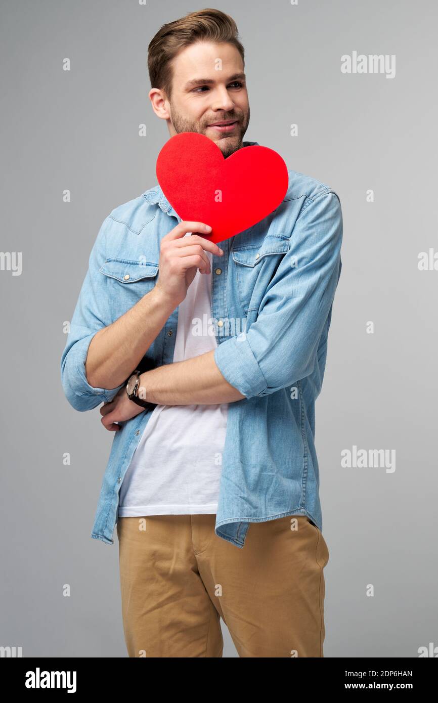 Ritratto di un uomo affascinante tenere mano carta a forma di cuore scheda indossa una camicia casual isolata su sfondo grigio Foto Stock