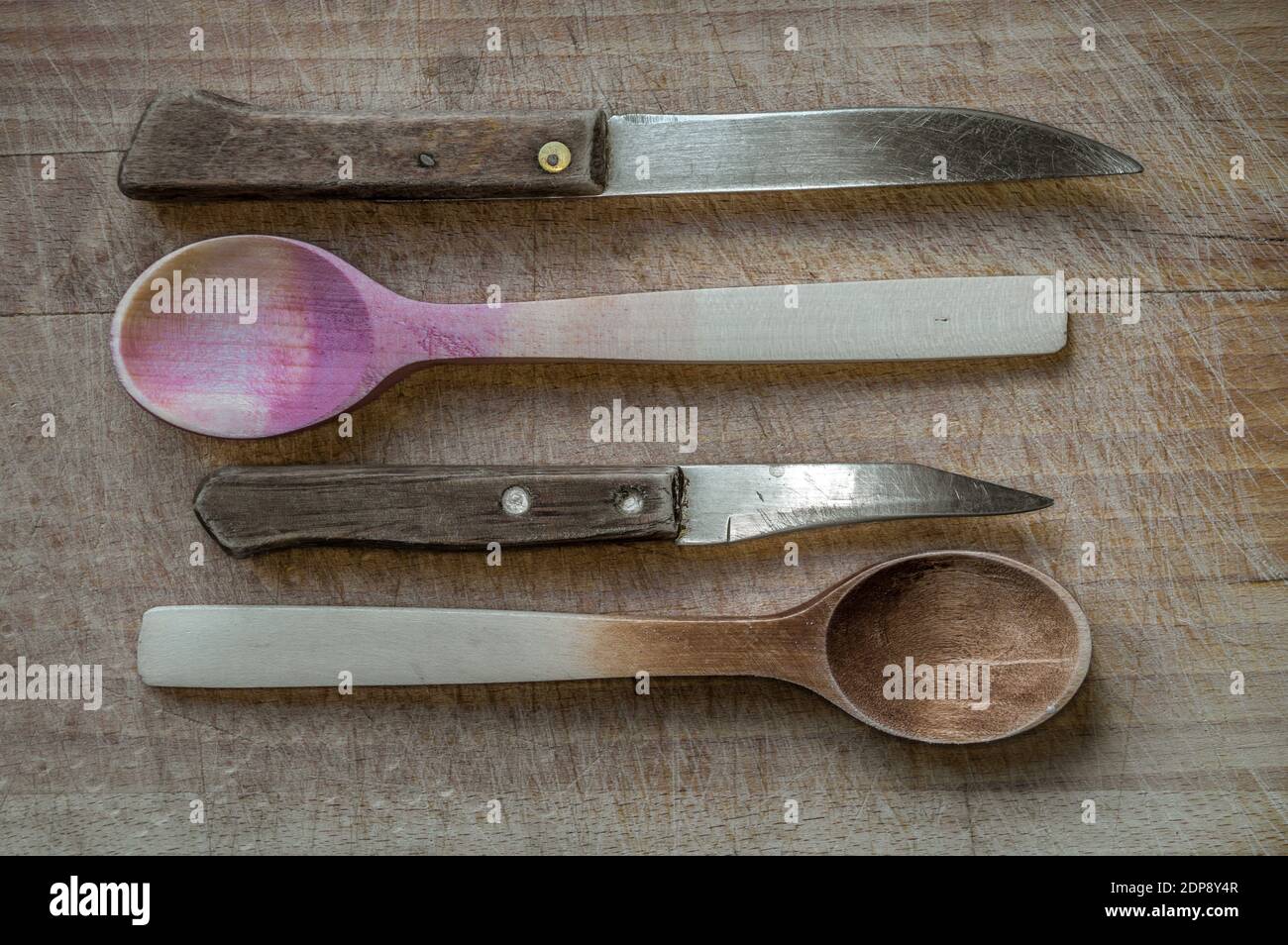 Una foto ad alto angolo di vecchi coltelli e cucchiai in legno su una superficie di legno Foto Stock