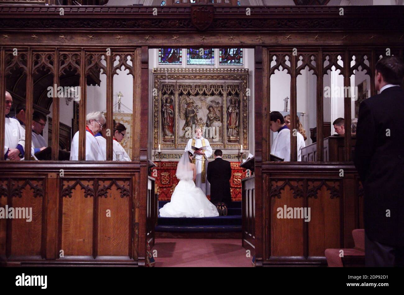 Sposa e sposo si inginocchiano per la benedizione in una cerimonia nuziale della chiesa cristiana con sposa in abito da sposa bianco. Con schermo rood, schermo coro o jube. Foto Stock