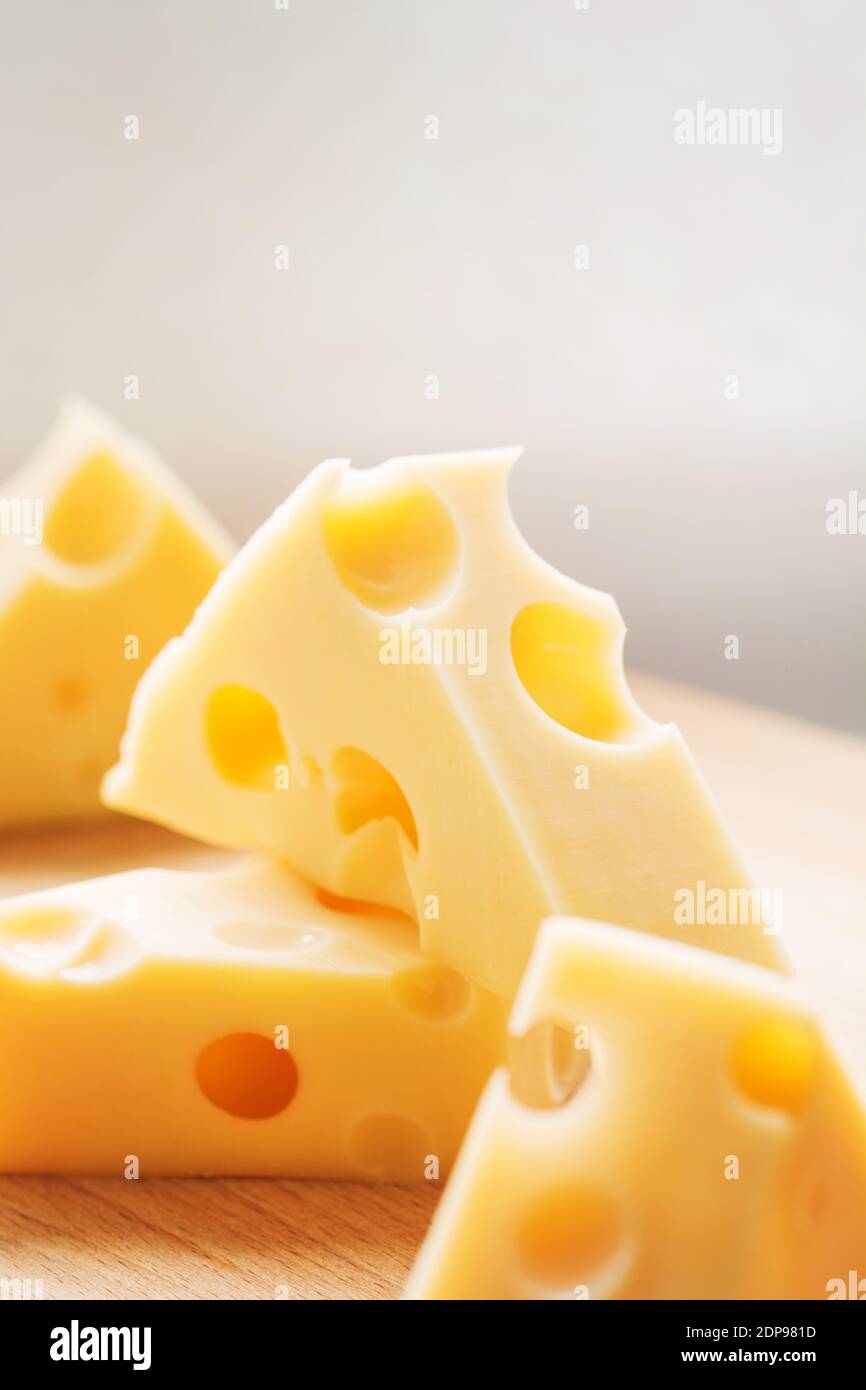 Pezzi triangolari di formaggio giallo svizzero con fori su piastra di legno. Formaggio di mucca olandese Maasdam Foto Stock