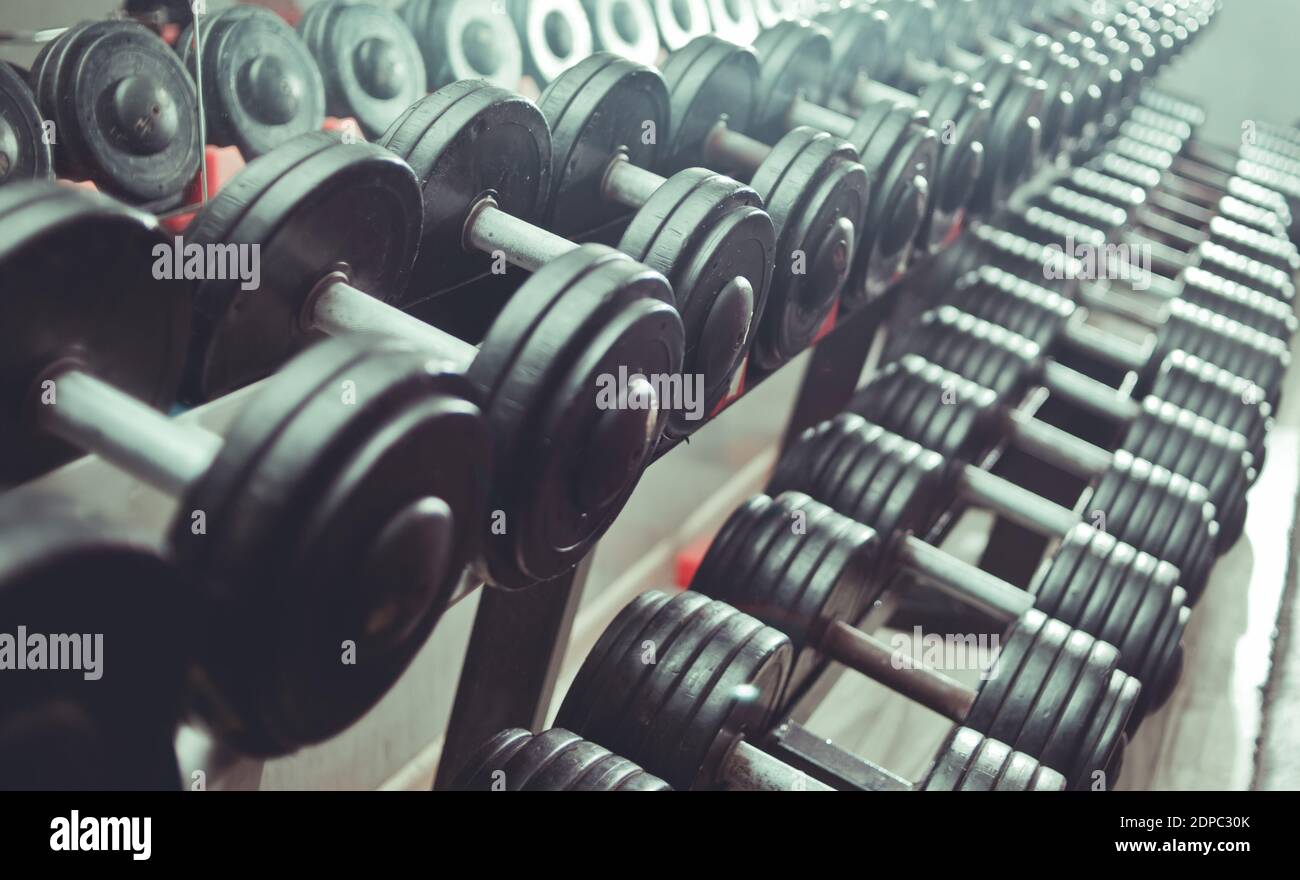 Chiudi molte manubri in metallo su rack nel centro fitness sportivo. Set di manubri neri. Foto Stock
