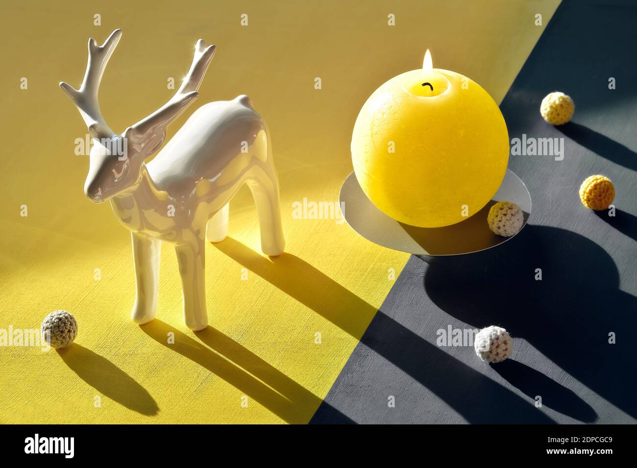 Luce solare, ombre lunghe, proiezione isometrica. Cervi, candele brucianti, fiori di cotone e palle su sfondo grigio giallo diviso. Illuminazione Foto Stock