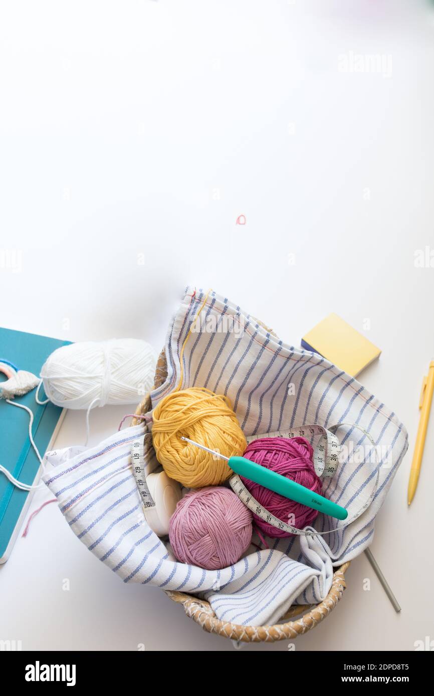 Vista dall'alto di alcune colorate palle di filato all'interno di un petto di vimini. Un ago da cucire verde e un misuratore da cucire sono nella parte superiore. Foto Stock