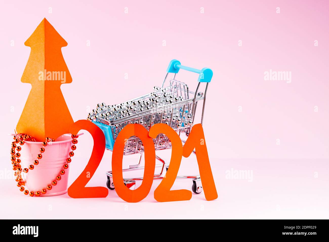 Albero di Natale rosso e l'iscrizione 2021 nel carrello. Decorazioni dell'albero di Natale nel carrello della spesa su sfondo rosa. Concetto di vacanza Foto Stock