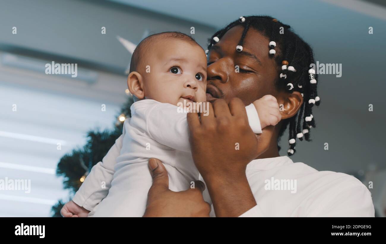 Tempo di Natale in famiglia multirazziale. Il padre nero afroamericano che tiene il suo bambino mulatto vicino all'albero di natale. Foto di alta qualità Foto Stock