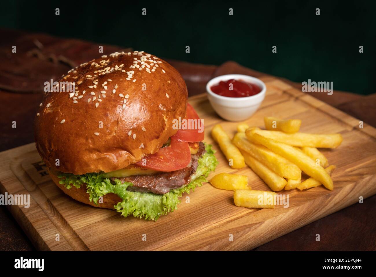 Hamburger di manzo fresco sono serviti con patatine fritte su un pannello decorativo di legno con salsa di pomodoro. Concetto di ristorante. Concetto di fast food. Cibo di strada Foto Stock
