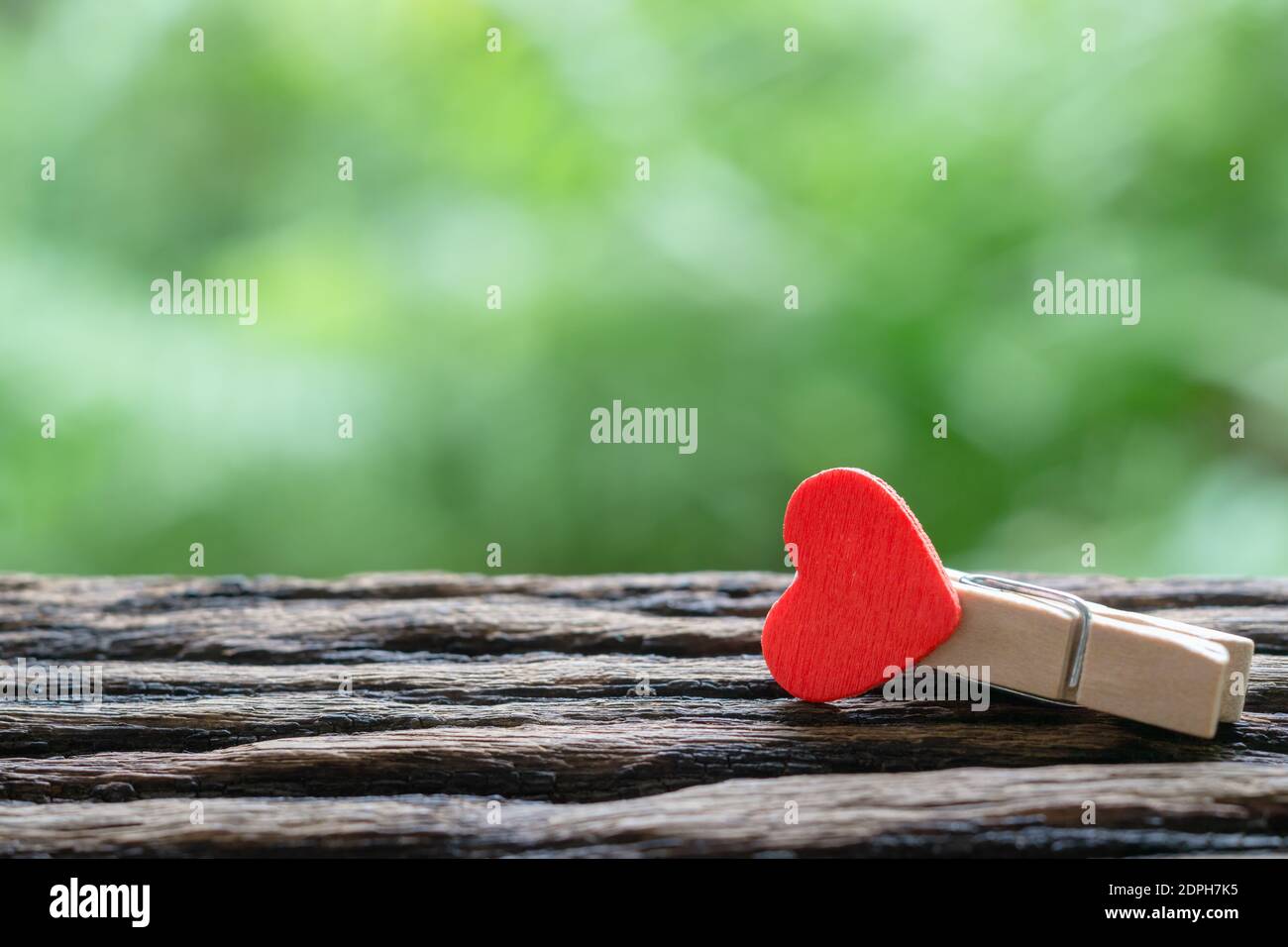 Primo piano fuoco selettivo delle clip di carta di legno di cuore rosso con sfondo verde della natura e spazio di copia. Ideale per giorno di San Valentino, Amore e concetto di relazione. Foto Stock