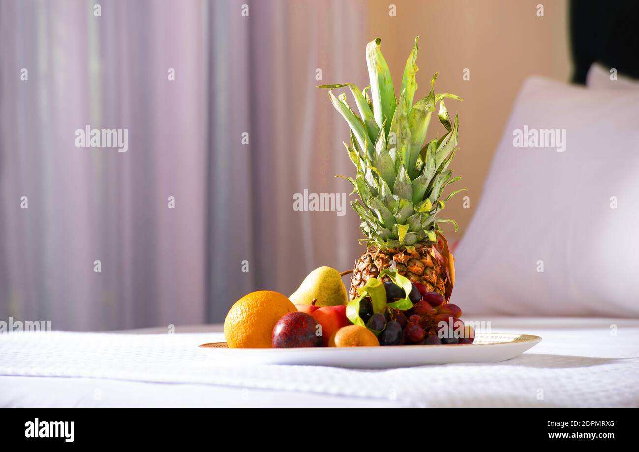 Primo piano di frutta con ananas su letto bianco sullo sfondo interno della camera da letto dell'hotel Foto Stock
