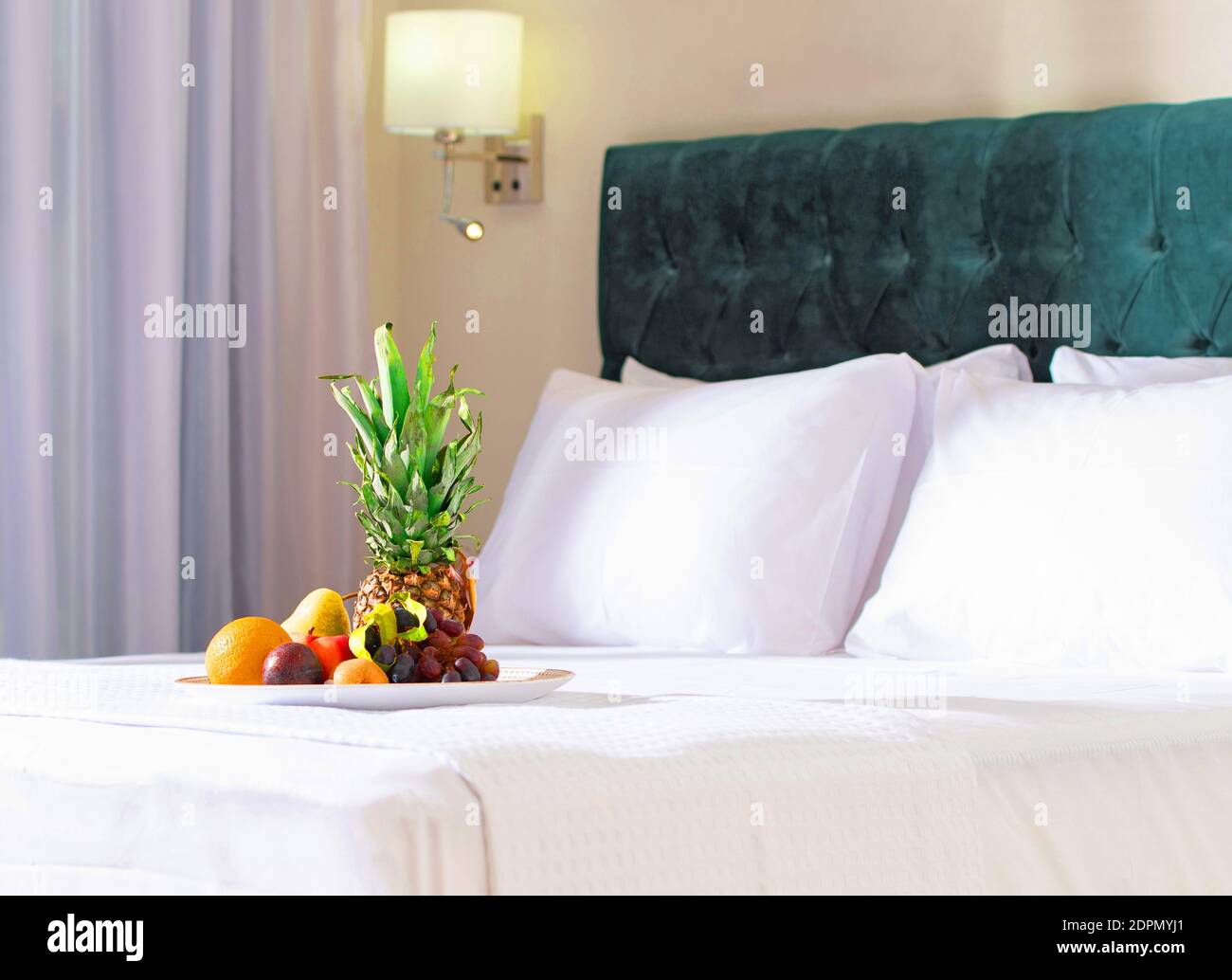 Omaggio di benvenuto fruttato nell'interno dell'hotel sfocato sfondo. Primo piano di sano piatto di frutta prima colazione con ananas su biancheria da letto bianca in camera da letto moderna. Foto Stock