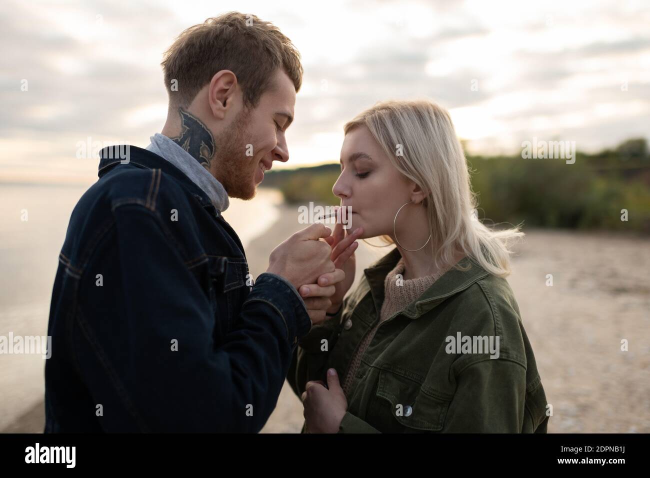 Vista laterale di allegro giovane hipster sorridente e di luce cannabis giunto per donna bionda mentre si è in piedi sulla costa del lago durante data in campagna d'autunno Foto Stock Vista laterale di allegro giovane hipster sorridente e di luce cannabis giunto per donna bionda mentre si è in piedi sulla costa del lago durante data in campagna d'autunno Foto Stock