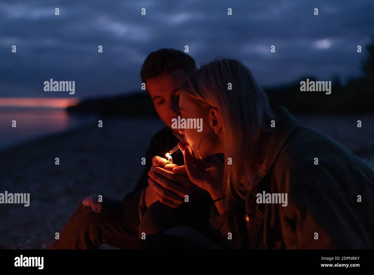 Giovane uomo che illumina la sigaretta di cannabis per la ragazza mentre si siede autunno natura e riposo di notte Foto Stock
