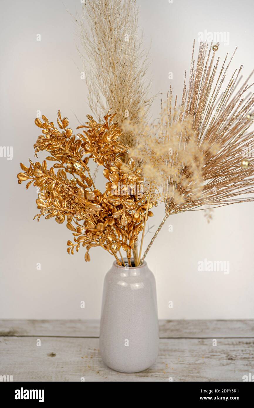 Composizione di erba di pampas con decorazione di rametto dorato di  Capodanno in un vaso su una parete bianca e sfondo di tavola di legno.  Arredamento di stile per le vacanze. Foto
