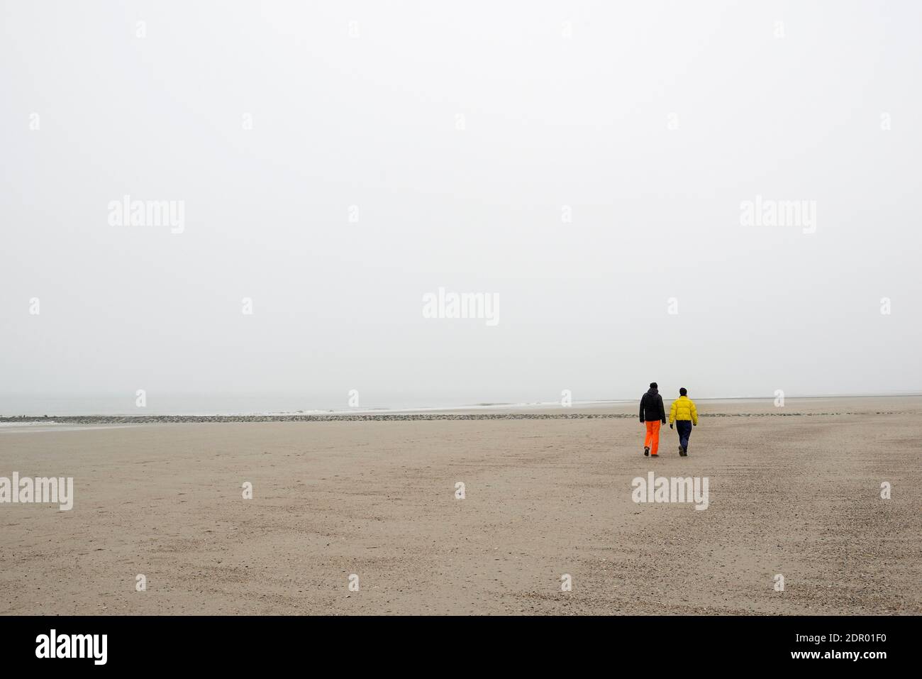 Due persone che camminano su una spiaggia sabbiosa in nebbia, Mare del Nord, Norderney, bassa Sassonia, Germania Foto Stock