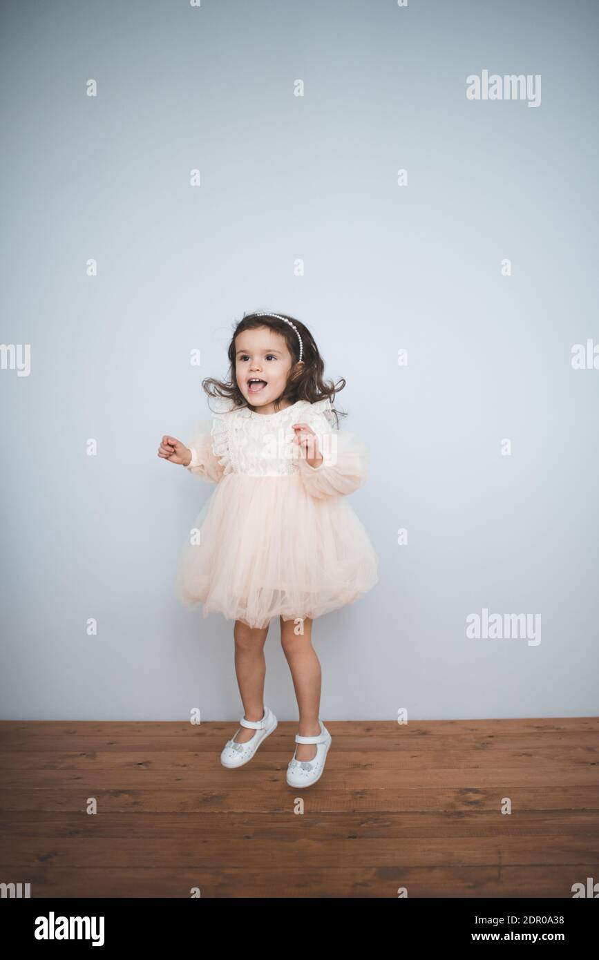 Sorridente ragazzina di 2-3 anni indossando elegante principessa vestito saltando e divertendosi da vicino all'interno. Guardando la fotocamera. Infanzia. Foto Stock