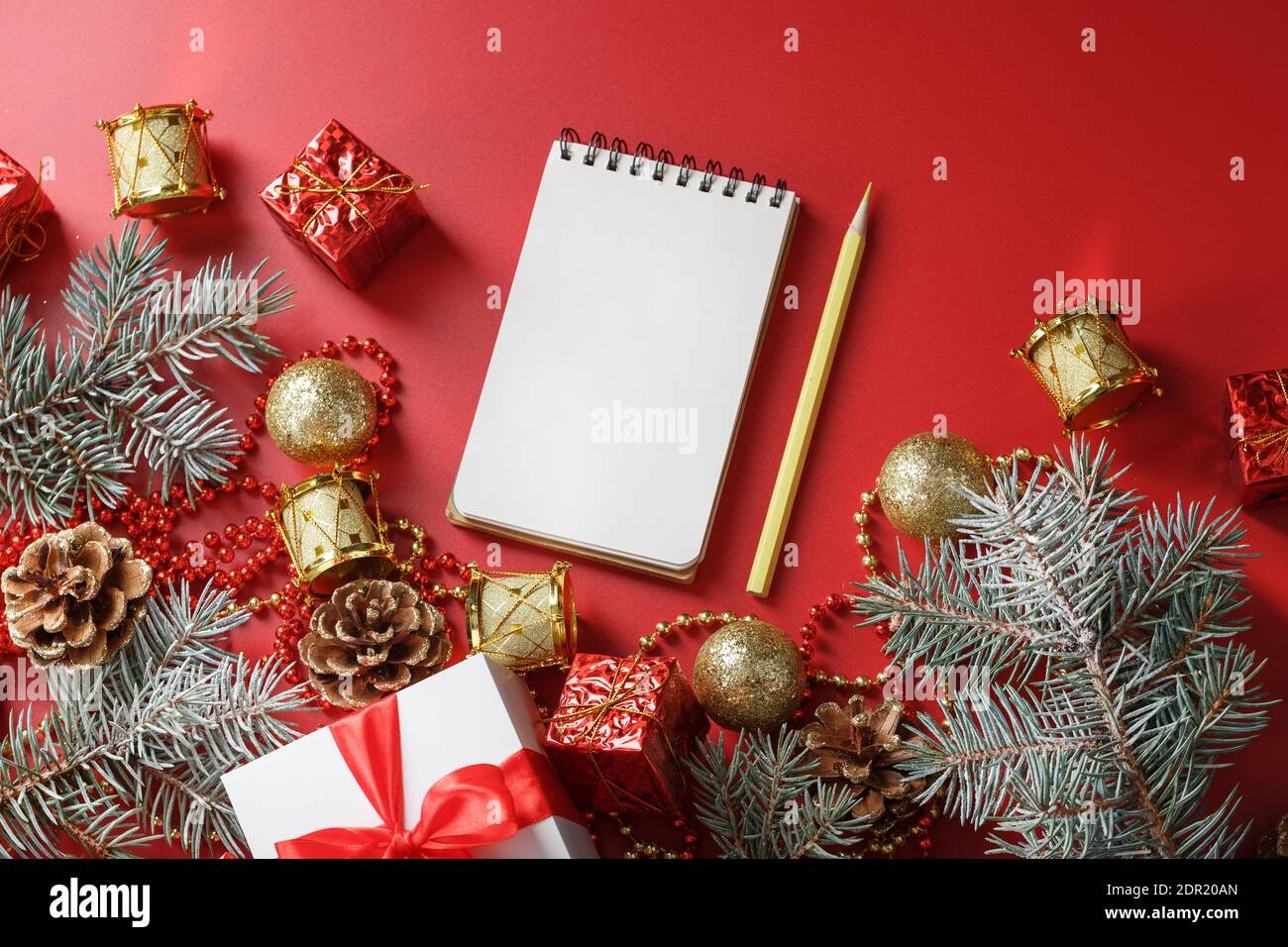 Composizione di Natale con blocco note e una matita per scrivere auguri con le decorazioni dell'albero di Natale su uno sfondo rosso. Umore di Natale e piani per t Foto Stock