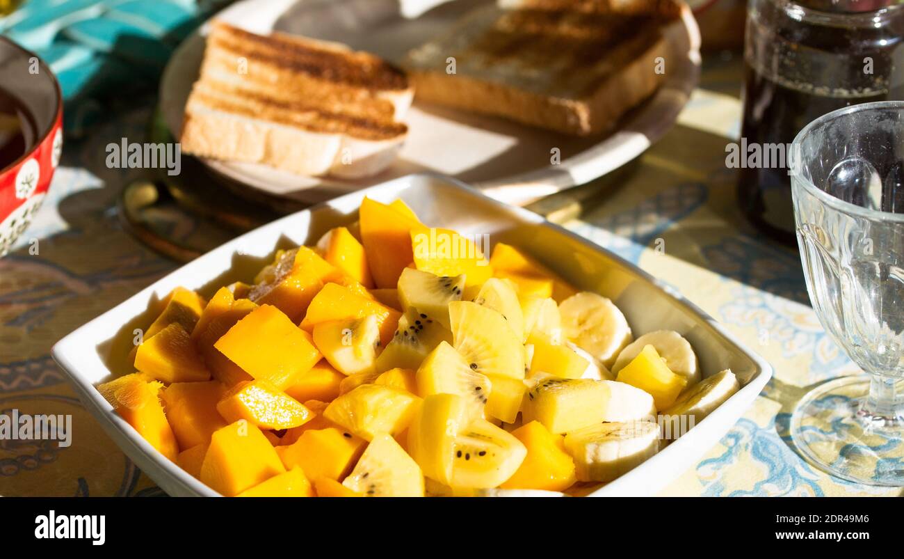 Grande piatto di frutta esotica fresca per colazione, mango, banane, kiwi dorato su un tavolo con pane tostato Foto Stock
