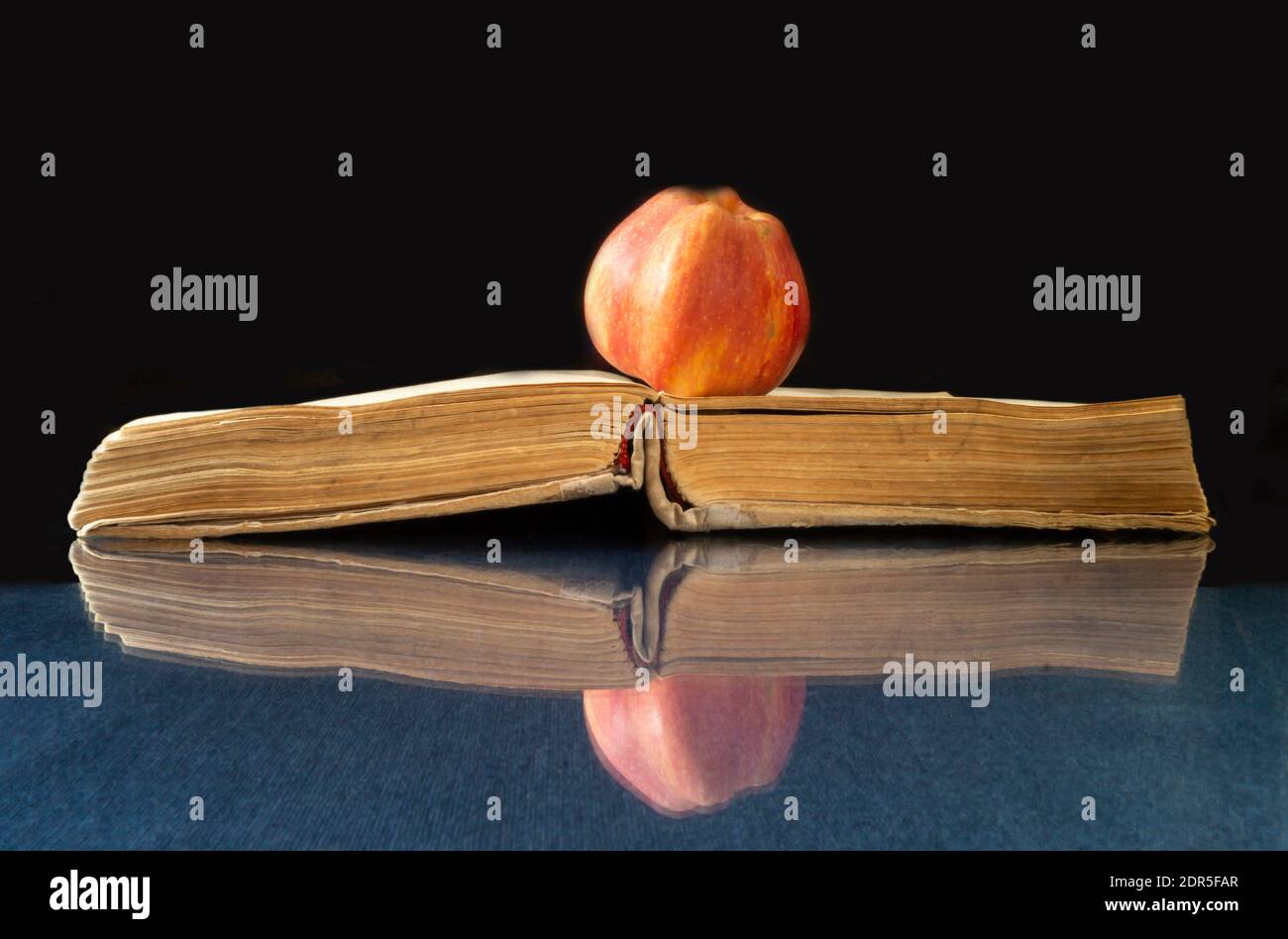 Il Libro e la mela poggia su un tavolo di vetro. Revealling libro con riflessione su sfondo nero Foto Stock