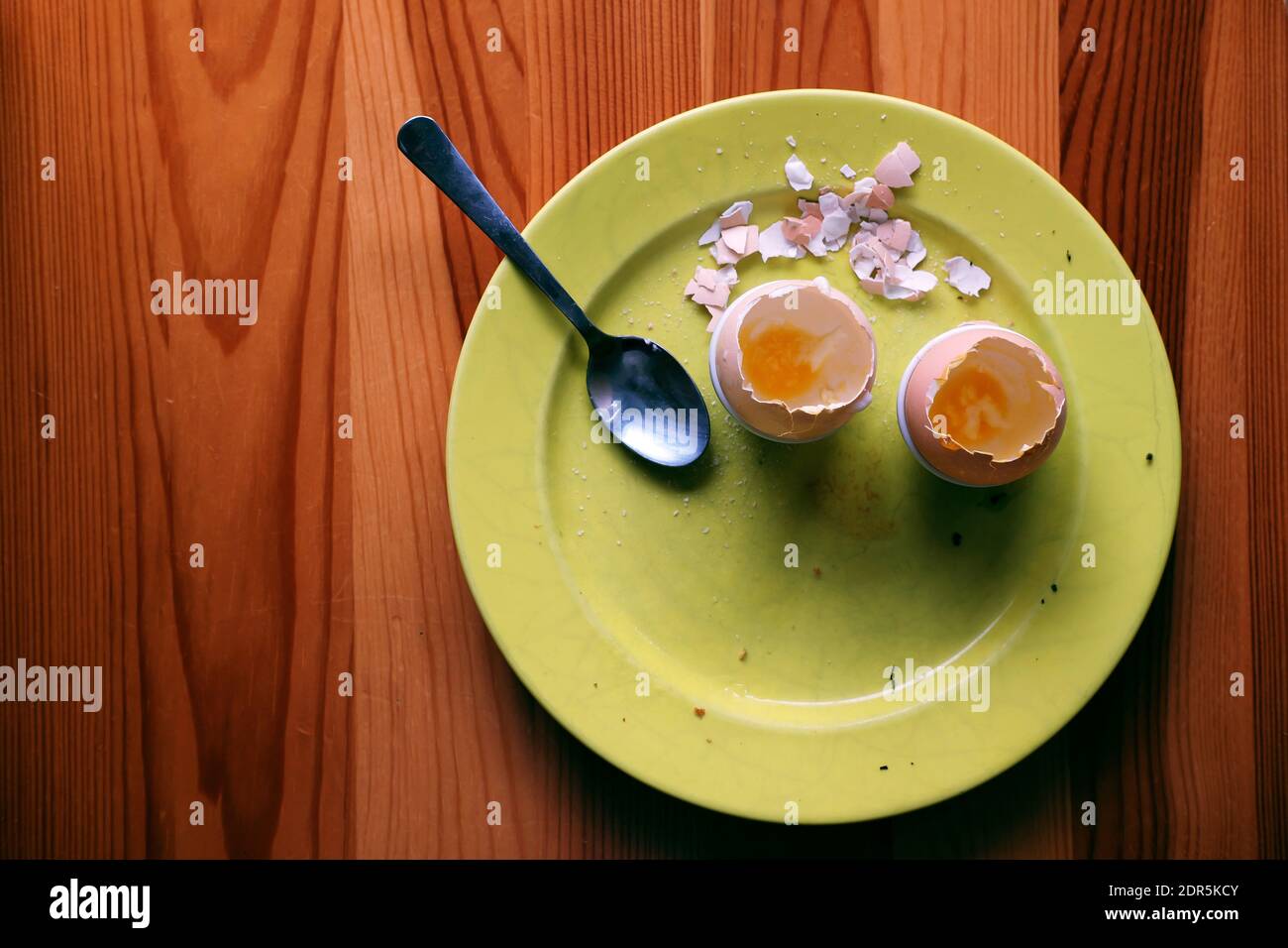 Dopo colazione - piatto giallo con gusci di gusci vuoti e spaccati e un cucchiaio lasciato su un tavolo di legno dopo un pasto Foto Stock